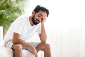 exhausted millennial eastern guy touching head after waking up